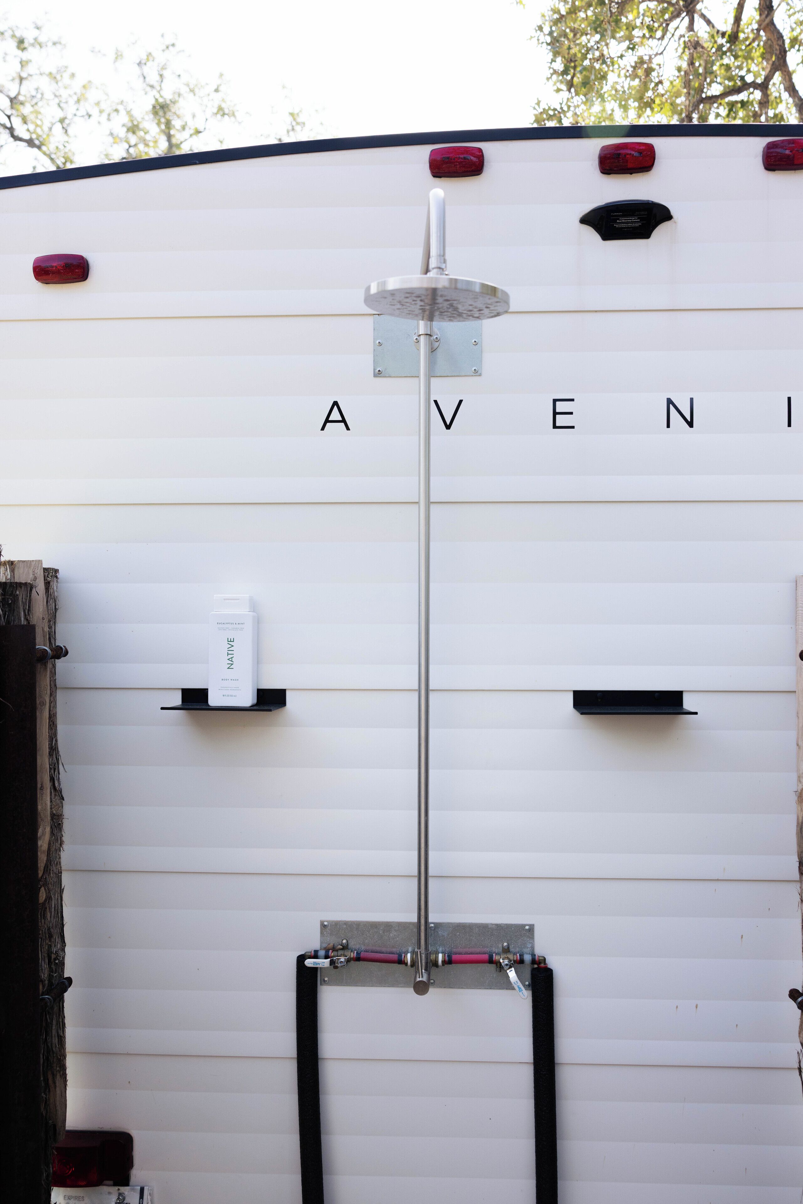 A white RV with the name "AVENI" on the side, a water spigot, and a shelf with a water bottle.