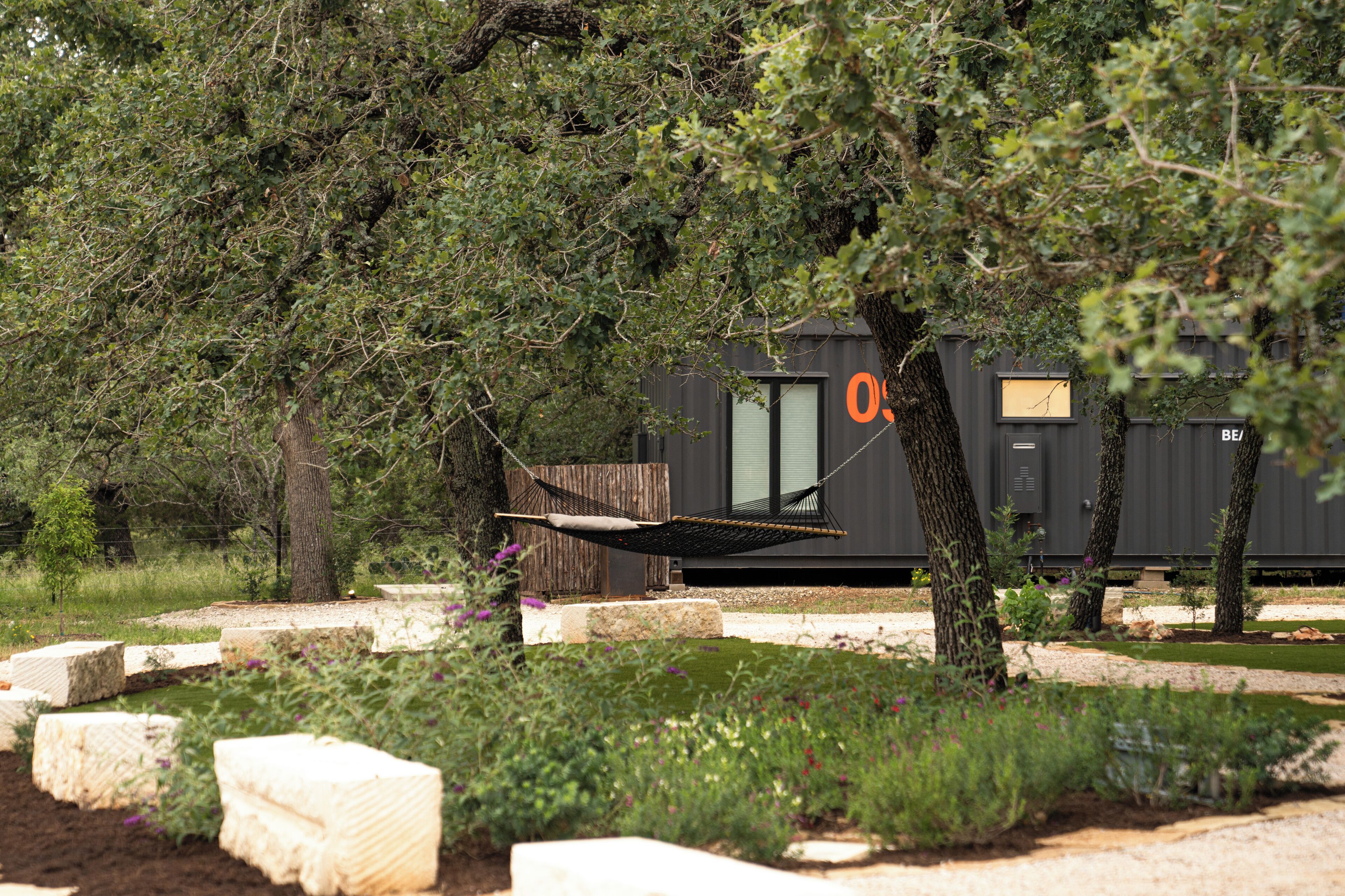 A modern outdoor area with a hammock, trees, and a building with a window.