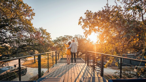 A wooden deck with metal railings, surrounded by trees and a sunset in the background. - ParcBlu (Fredericksburg)