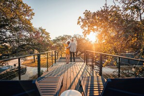 A wooden deck with metal railings, surrounded by trees and a sunset in the background. - ParcBlu (Fredericksburg)
