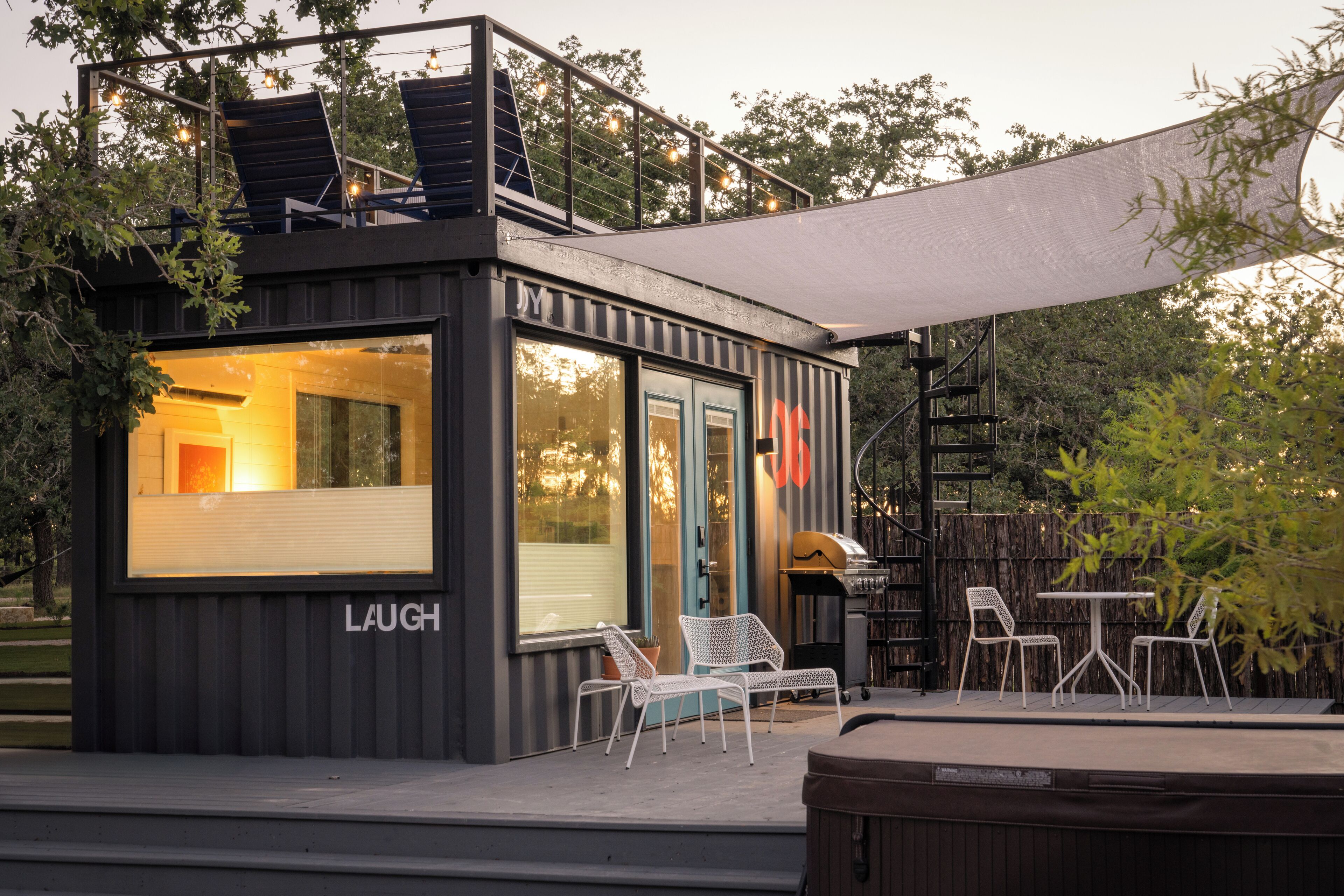 A compact, modern outdoor seating area with a grill and a covered table, surrounded by a wooden deck and trees.
