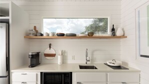 A modern kitchen with white cabinetry, a built-in microwave, a coffee maker, and a window above the counter. - ParcBlu (Fredericksburg)