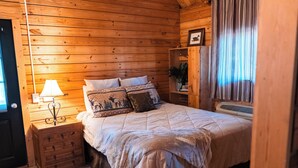 A wooden-paneled bedroom with a bed, a nightstand with a lamp, a dresser, and a window with curtains. - 2 Lakeside : Charming 2-bedroom cabin with AC, WiFi in welcoming Solgohachia (Solgohachia)