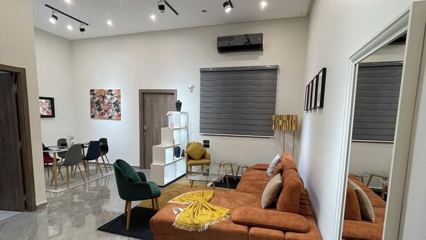 Una sala de estar moderna con un sofá modular, un comedor con sillas y un ventanal con persianas.