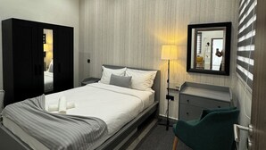 Una habitación de hotel moderna con cama, escritorio, silla, armario y espejo en la pared.