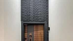 Un pasillo con una puerta moderna que presenta un diseño de panel de madera y un picaporte negro. Un felpudo colorido con la palabra