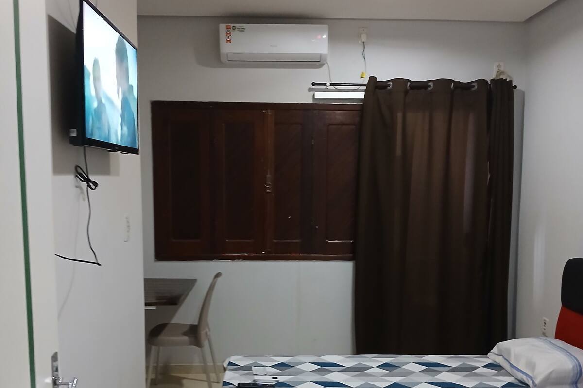 Ett sovrum med en säng, ett skrivbord, en stol, en tv och en luftkonditioneringsanläggning.
