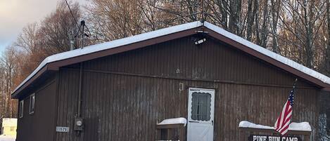 Une cabane en bois, dont le toit est recouvert de neige, avec une porte et un banc sur lequel est posé un drapeau américain.