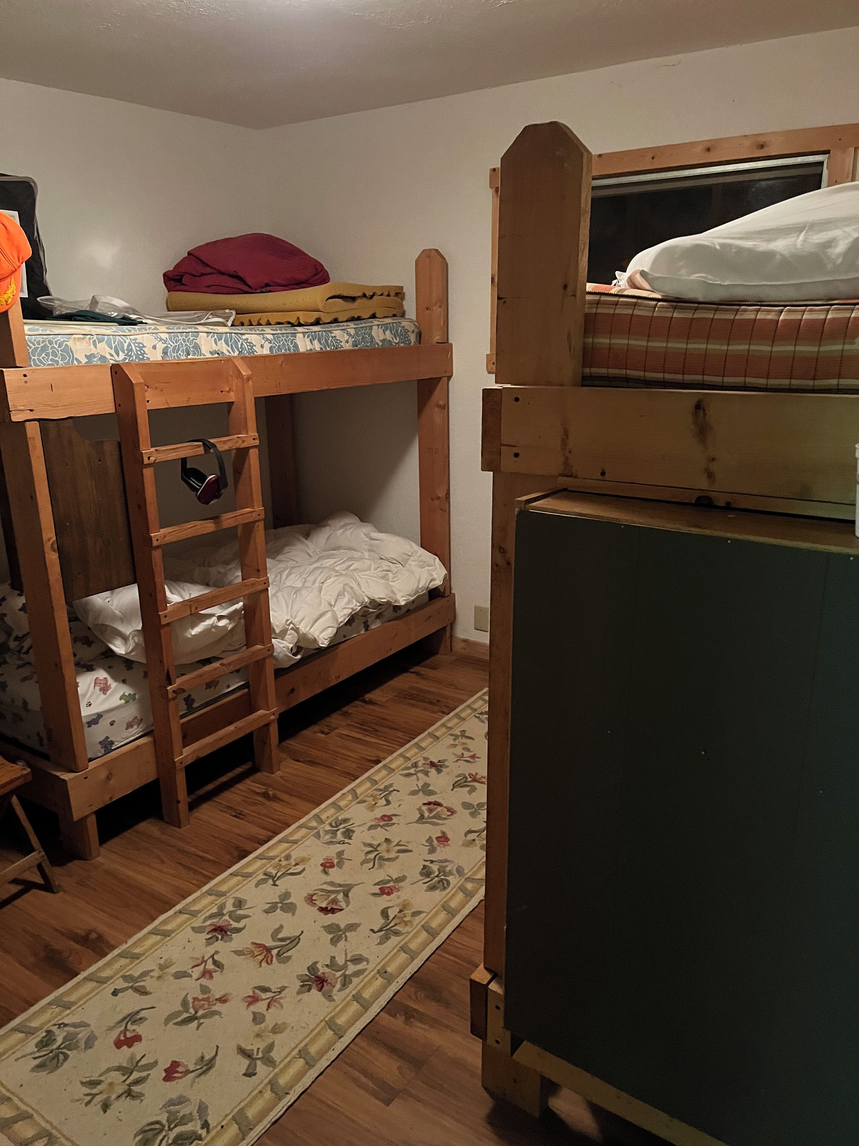 Quarto com duas beliches, uma escada de madeira, um tapete estampado com flores e uma pequena mesa.