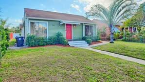 A single-story house with a red door, green siding, and a small front yard.