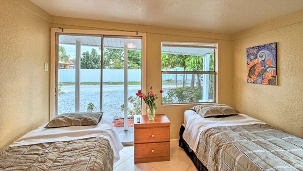 A room with two beds, a wooden nightstand, a vase with flowers, and a painting on the wall.