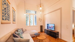 Moderni olohuone, jossa on sohva, pyöreä sohvapöytä, televisio ja taideteoksia seinillä.