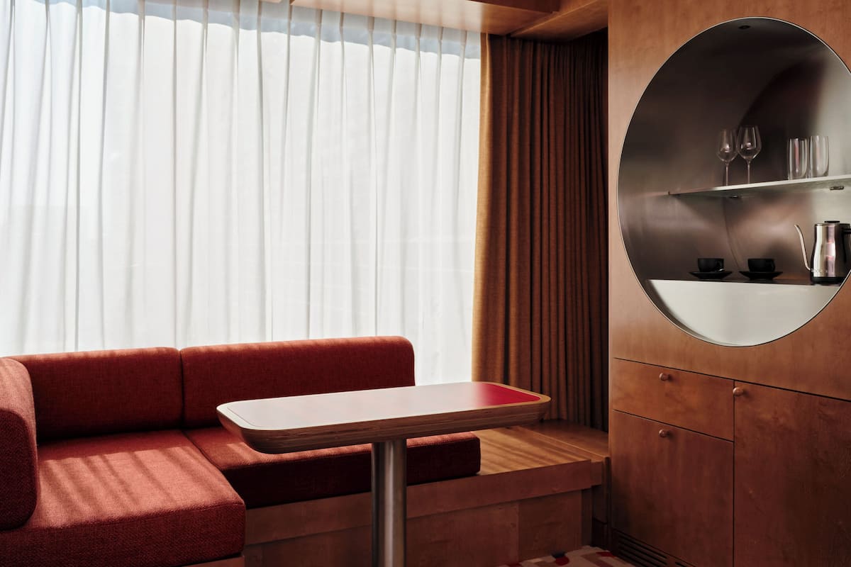 Un interior moderno con un sofá rojo, una pequeña mesa y una zona de cocina integrada con un espejo redondo.