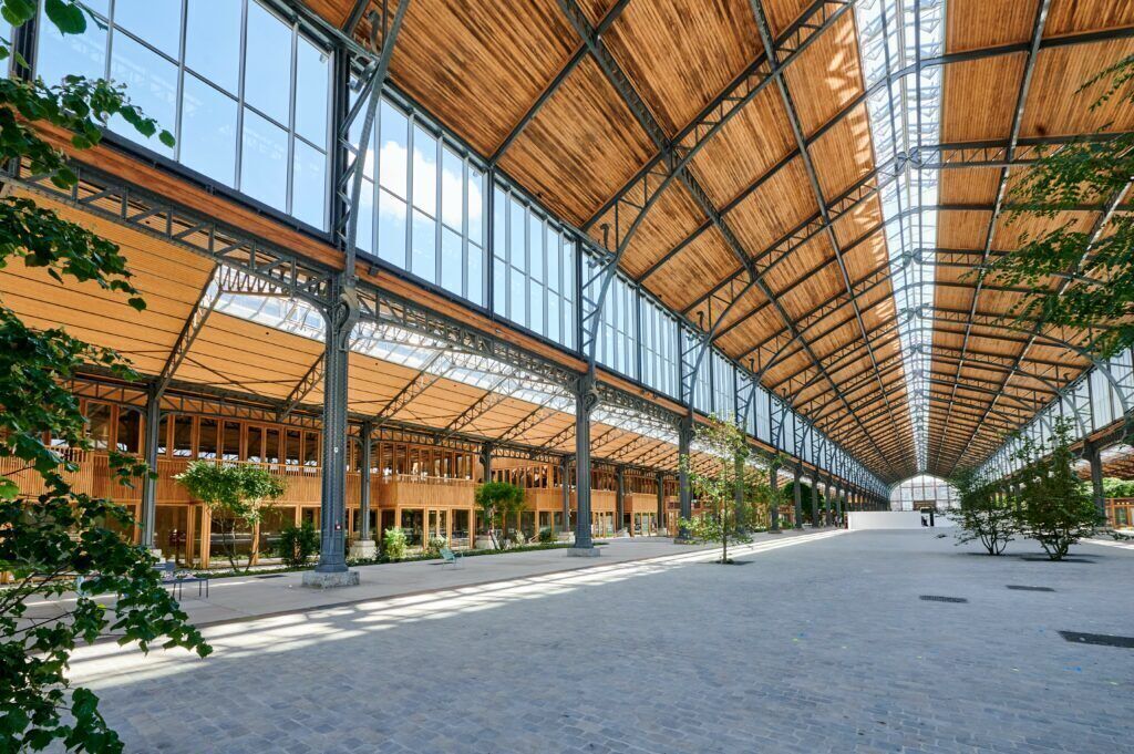 A spacious indoor area with a high ceiling and large windows, featuring a wooden structure and columns.