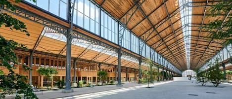 A spacious indoor area with a high ceiling and large windows, featuring a wooden structure and columns.