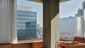 A modern interior with a large window offering a city view, a wooden bench, and a metal-framed chair. - The Standard Brussels (Brussels)