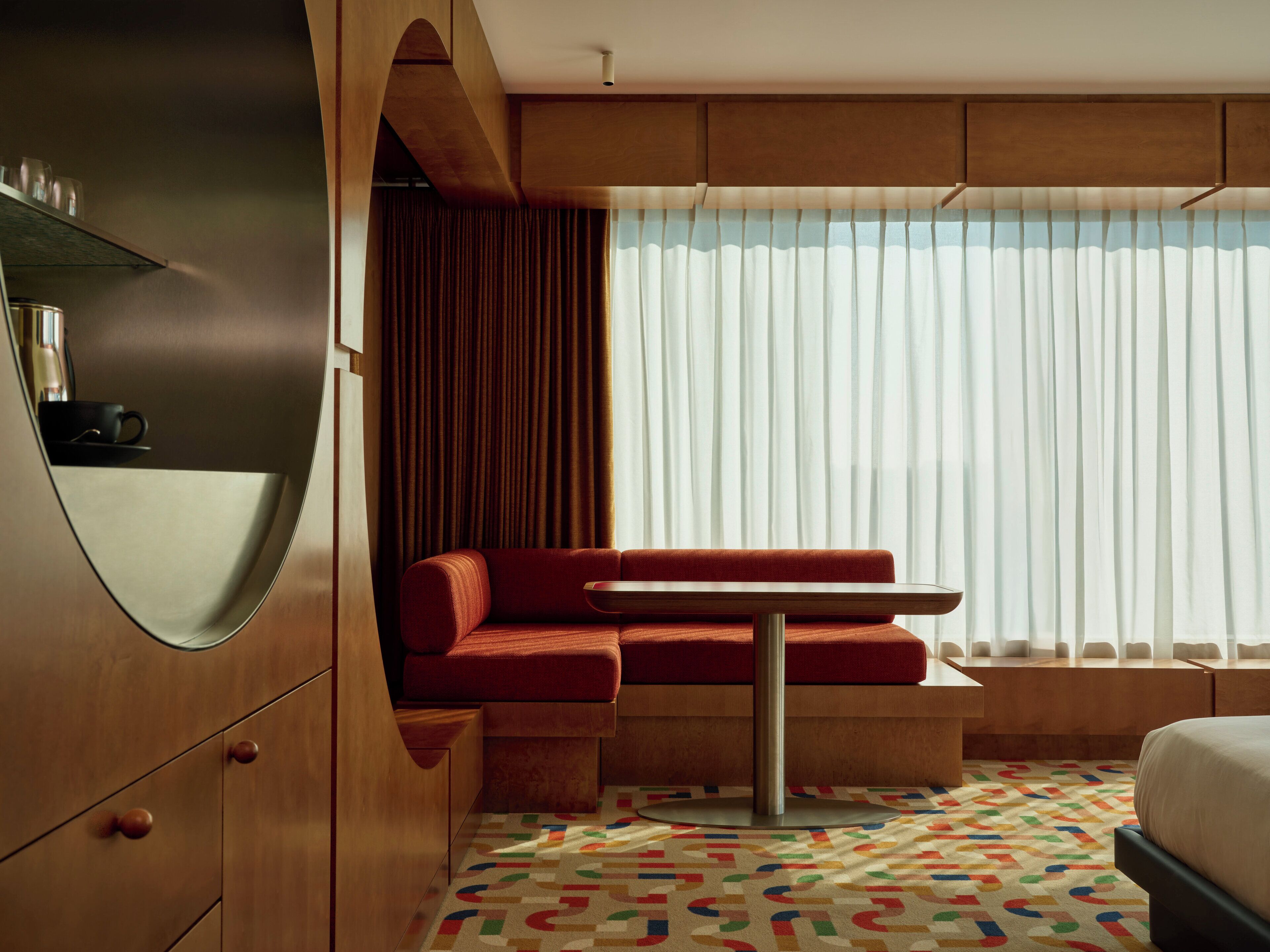 A modern room with a red sofa, a small table, and a large window with sheer curtains.