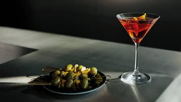 A martini glass with a lemon slice on a reflective surface, next to a plate of olives.