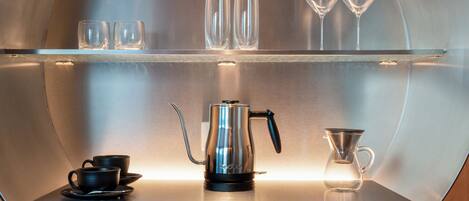 Un interno circolare in metallo con una macchina del caffè, due tazze e due bicchieri da vino su un ripiano.