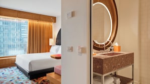 A hotel room with a bed, a bedside table, a window with curtains, a bathroom with a sink and mirror, and a tiled floor. - The Standard Brussels (Brussels)