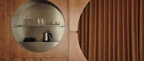 A circular mirror with a shelf above it holding glasses and a coffee pot.