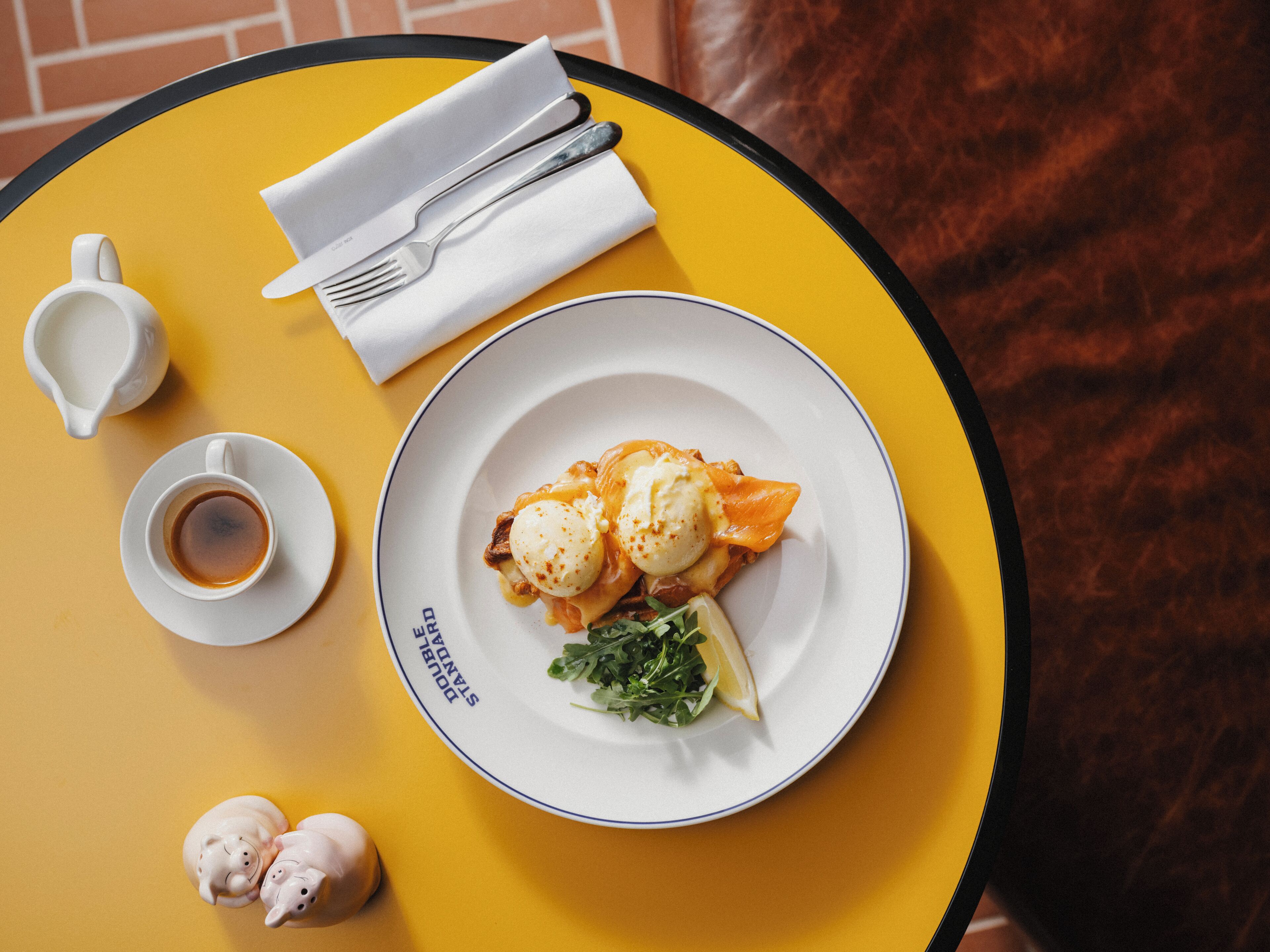 A table with a plate of food, a cup of coffee, and a napkin with cutlery.