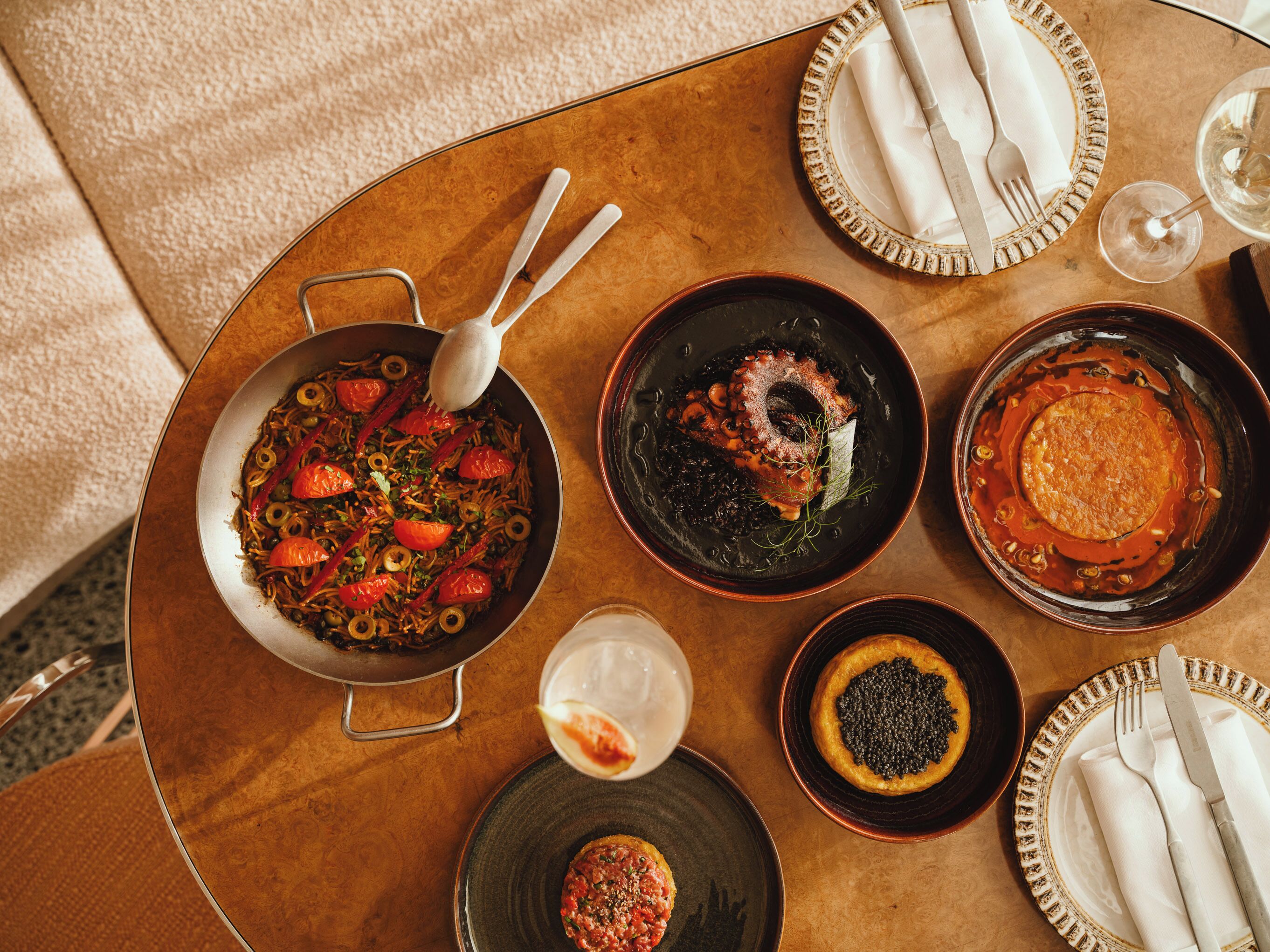 Una mesa de comedor con varios platos, incluyendo una sartén de vegetales salteados, un tazón de sopa y un plato con caviar.