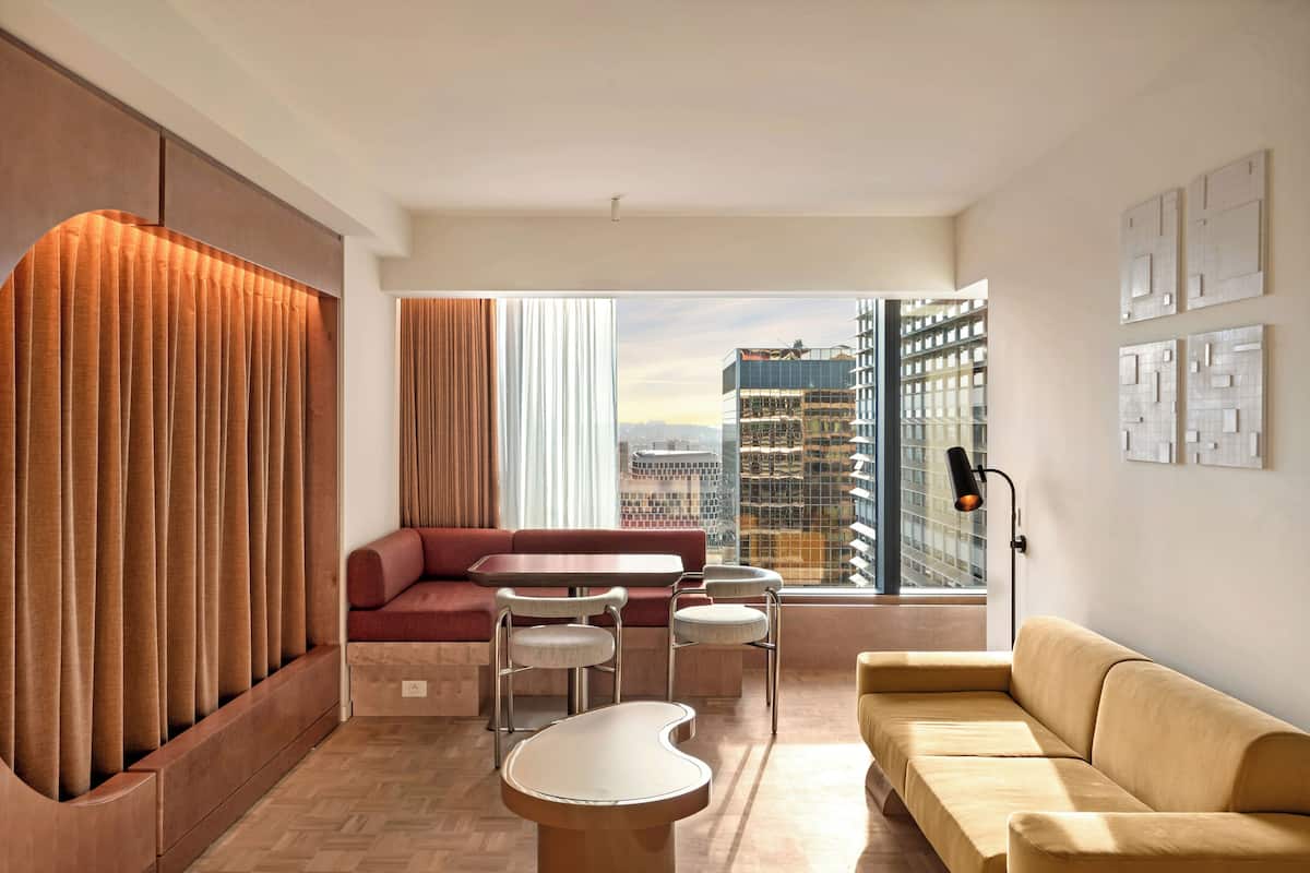 Una sala de estar moderna con sofá, sillas, una mesa y vistas a un paisaje urbano a través de amplios ventanales.