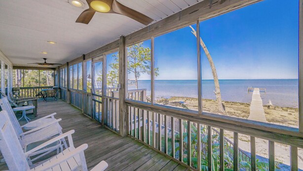 A covered porch with white chairs, a ceiling fan, and a view of the beach. - Bayside 3 bedroom Bungalow (Gulf Shores)
