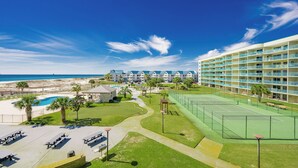 Un complejo turístico con cancha de tenis, piscina y vista al mar.