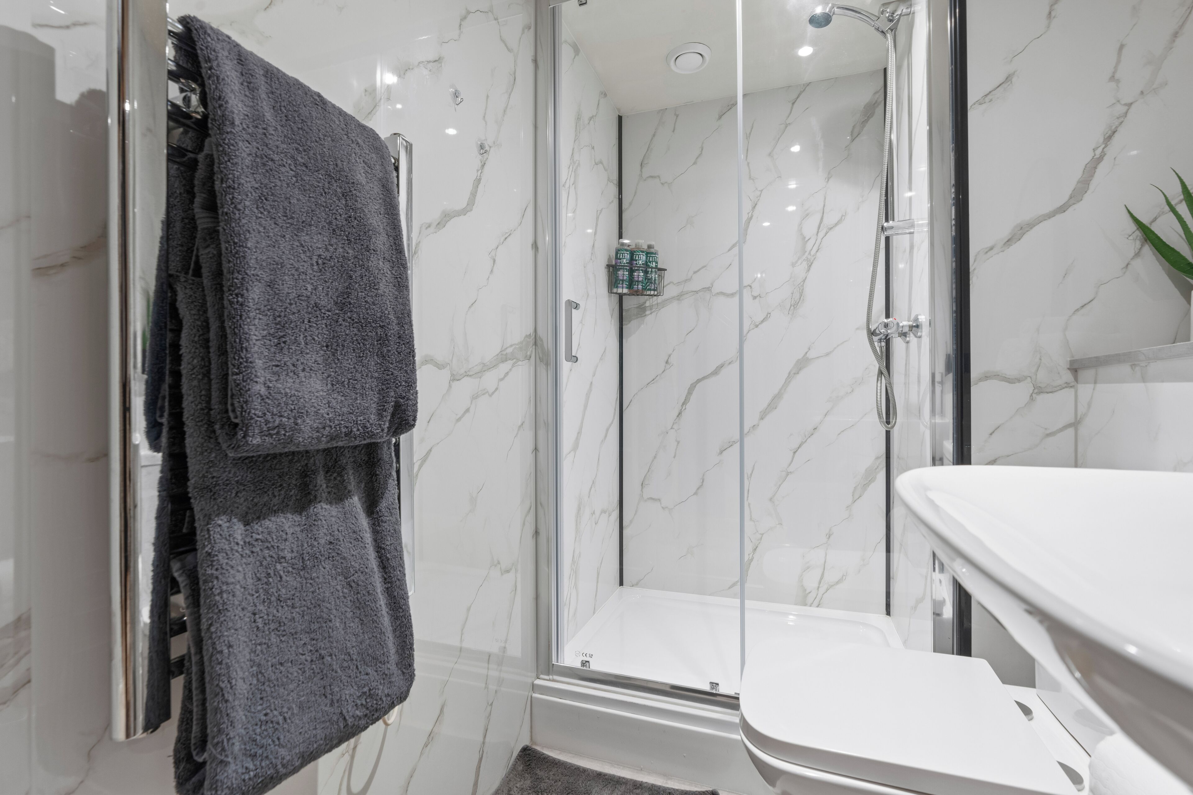 Un baño moderno con ducha de vidrio, lavamanos blanco y toallero con una toalla doblada.