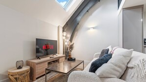 A modern living room with a flat-screen TV displaying 'NETFLIX', a wooden TV stand, a coffee table, a sofa, and a decorative vase.
