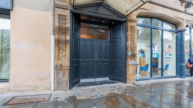 A building entrance with a dark door, a stone wall, and a glass door with chairs inside.