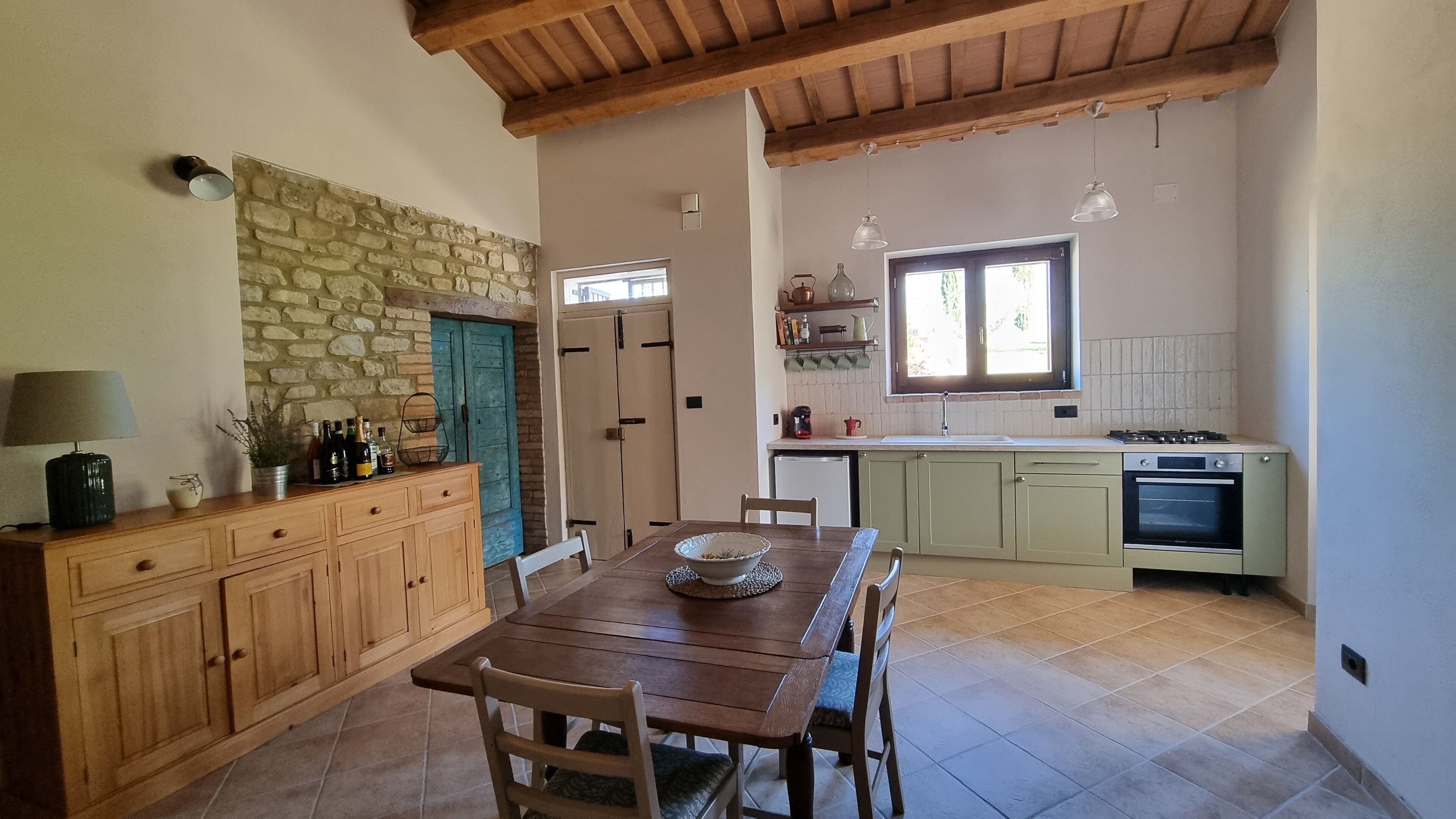 A kitchen with a stone wall, wooden cabinets, a dining table with chairs, and a window.