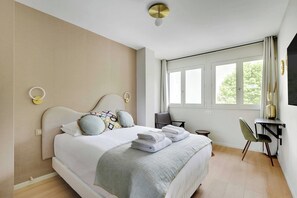 A modern bedroom with a large bed, bedside tables, a desk, and a window with curtains.