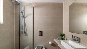 Ein modernes Badezimmer mit einer Glaskabine zur Dusche, einer weißen Toilette und einem großen Spiegel über einem weißen Waschbecken.