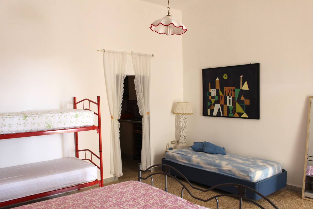 Une chambre avec des lits superposés, un bureau, une lampe et une œuvre d’art géométrique accrochée au mur.