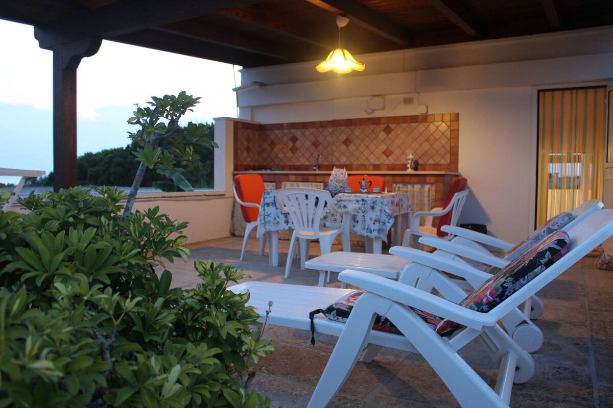 Un espace extérieur aménagé, abrité et doté de fauteuils confortables et d’une table, le tout entouré de verdure.