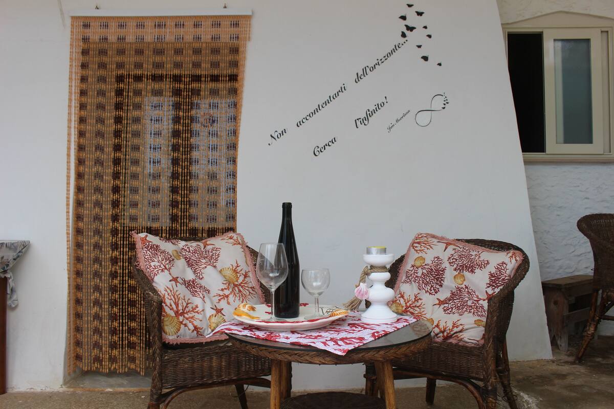 Une table à manger avec deux chaises en osier, une bouteille de vin et une assiette de nourriture.