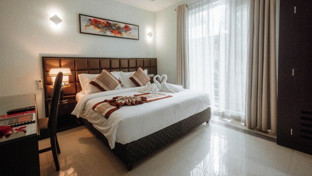 A hotel room with a large bed, a desk with a lamp, a chair, and a wardrobe. - Viveka Hotel Colombo (Colombo)