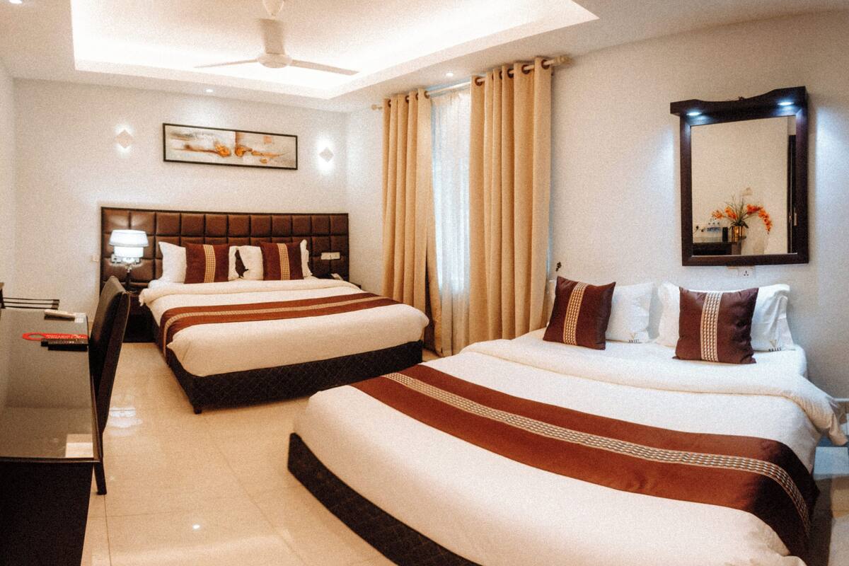 A hotel room with two beds, a desk, a chair, a lamp, a ceiling fan, and a large mirror.