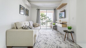 A modern living room with a sofa, a small table with a plant, and a view to the outside.