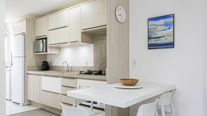 A modern kitchen with white cabinets, a white countertop, and a dining area with white chairs.