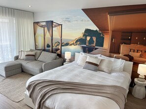 Quarto de hotel com cama, sofá, vista para uma paisagem montanhosa e piscina.