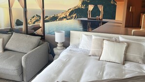 A bedroom with a bed, a seating area with a chair, a nightstand, and a view of a mountainous landscape through a window. - Bay View Motel - Sunrise (Lorne)