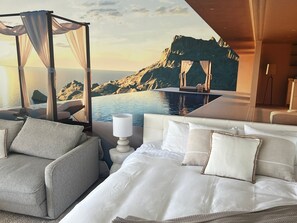 A bedroom with a bed, a seating area with a chair, a nightstand, and a view of a mountainous landscape through a window.