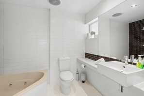 A modern bathroom with a bathtub, toilet, and a sink area with a mirror and toiletries.
