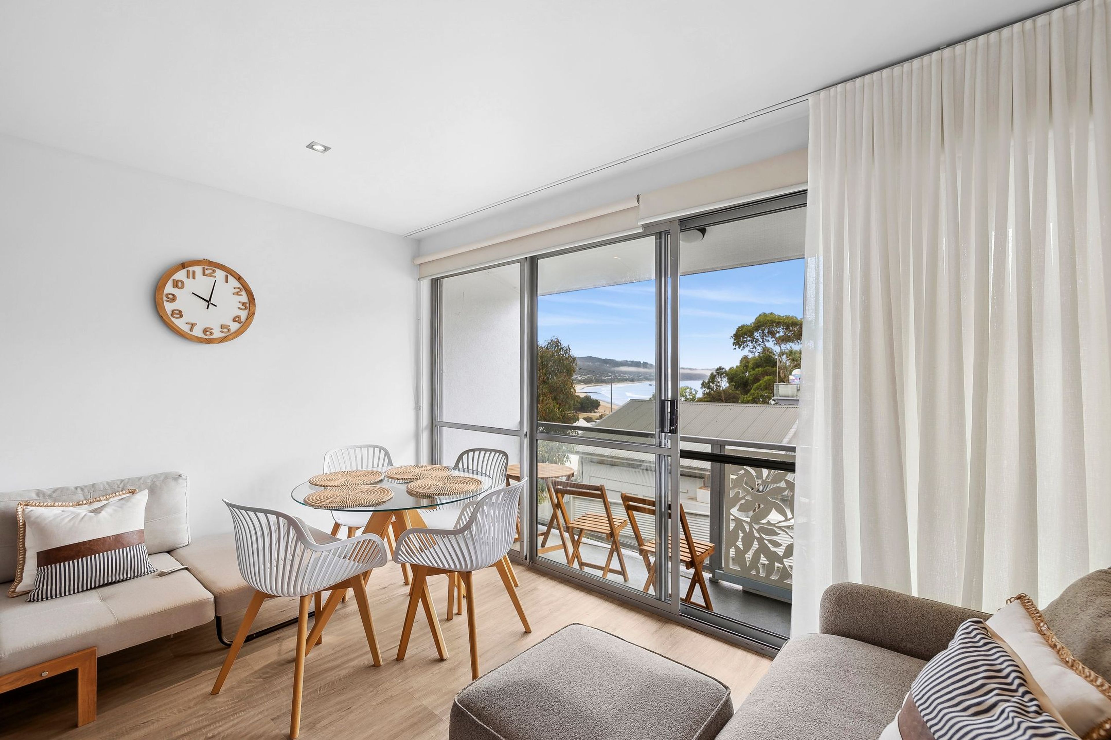 Een moderne woonkamer met balkon, een eethoek met ronde tafels en een groot raam met uitzicht.