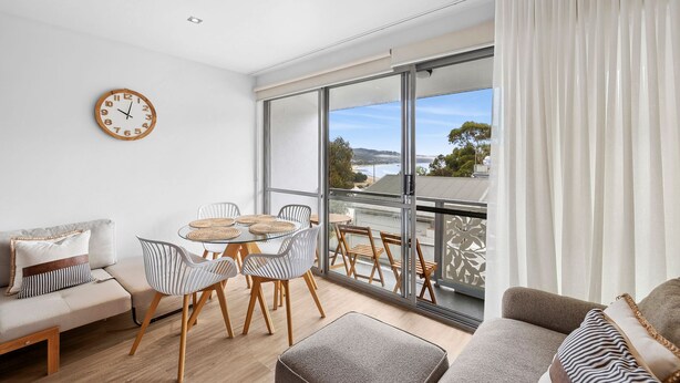 A modern living room with a balcony, a dining area with round tables, and a large window with a view. - Bay View Motel - Sunrise (Lorne)