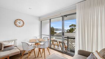 Een moderne woonkamer met balkon, een eethoek met ronde tafels en een groot raam met uitzicht.